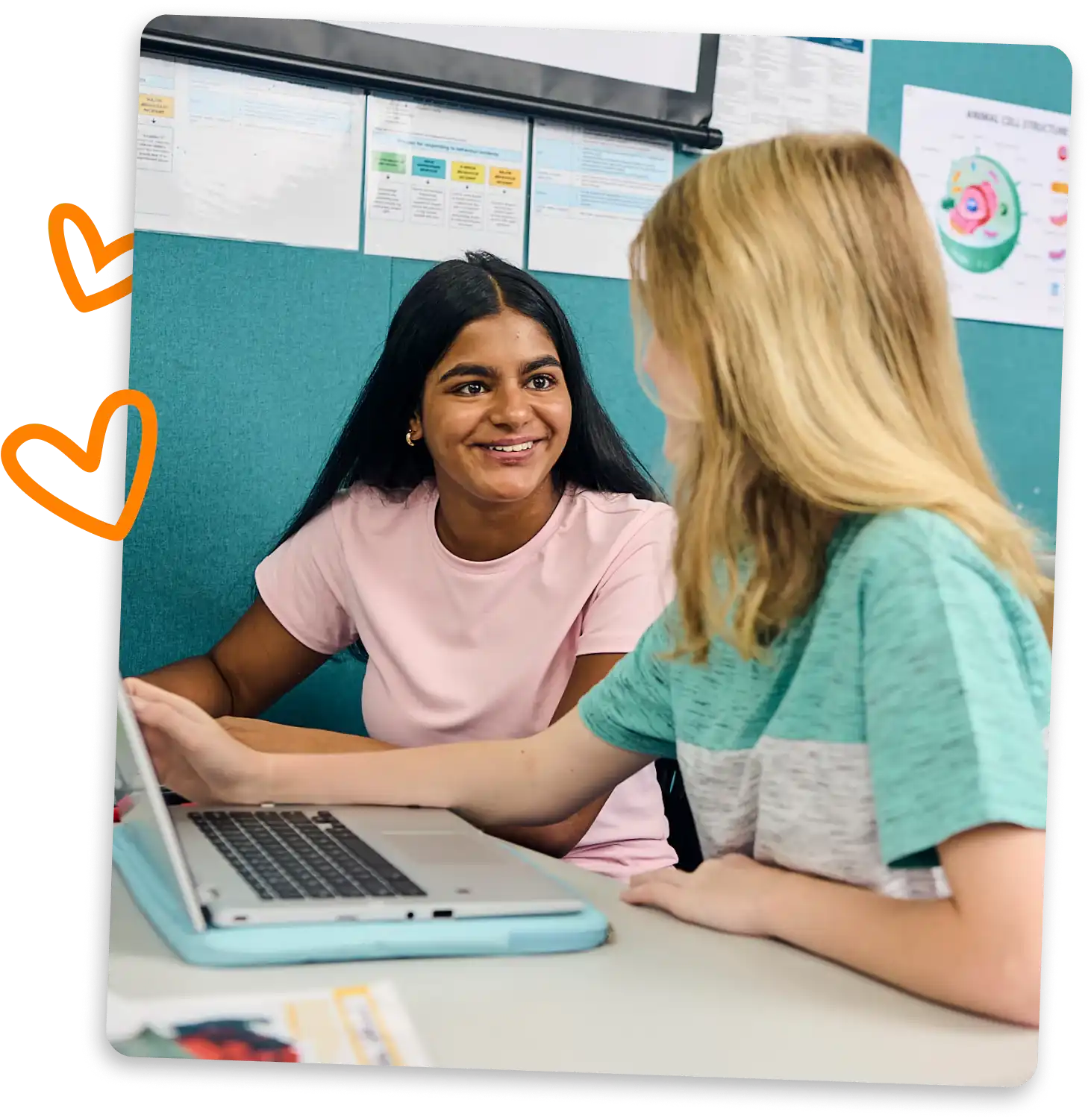 Two students sit at a desk in a classroom, smiling and talking. One is using a laptop, and there are colorful charts on the wall behind them. Orange doodle hearts are drawn on the left side of the image.