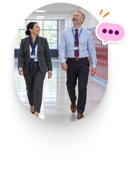 Two school leaders smiling as they walk and talk down a school hallway.