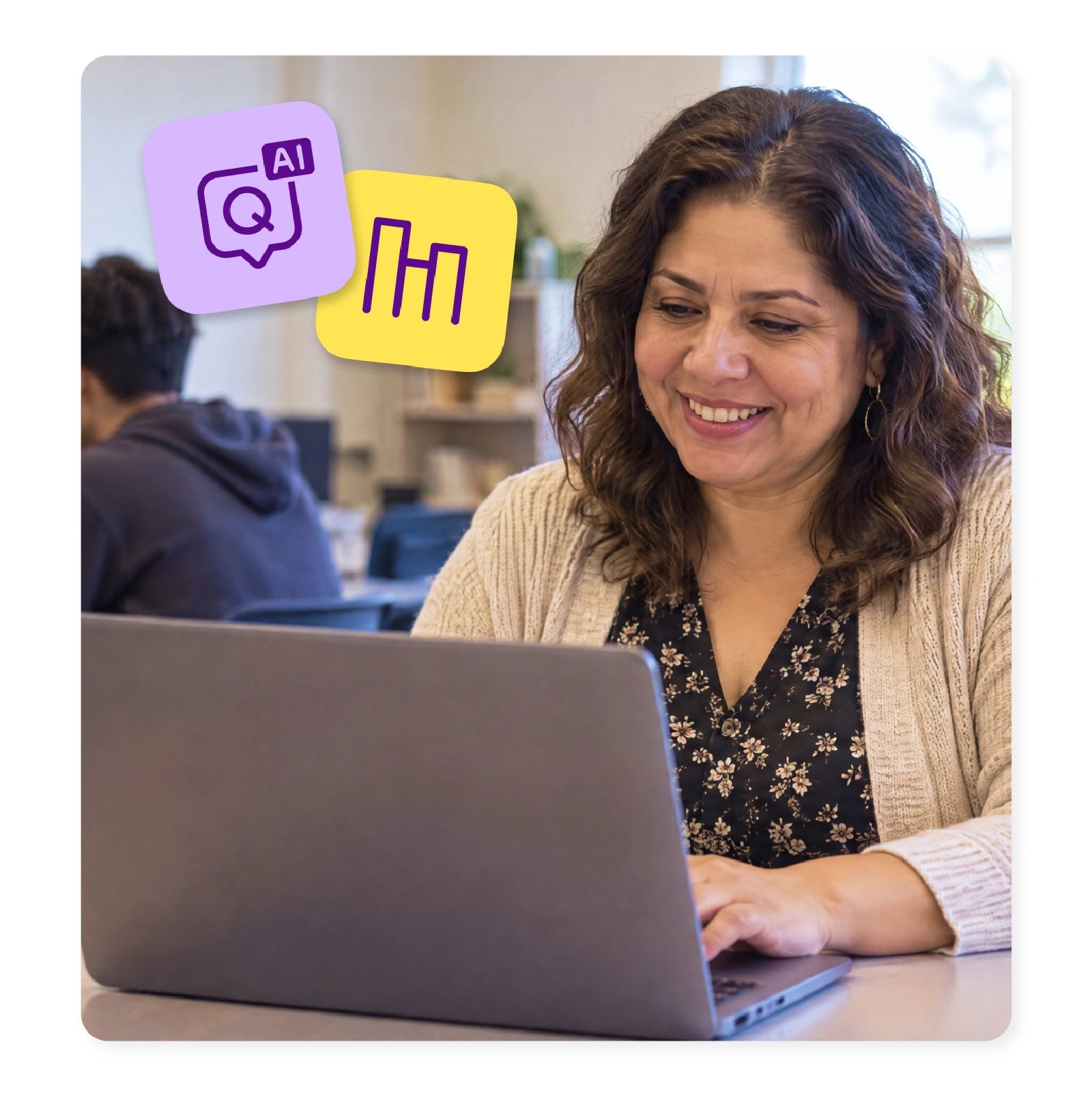 A teacher smiles at her laptop as students work around her in class.