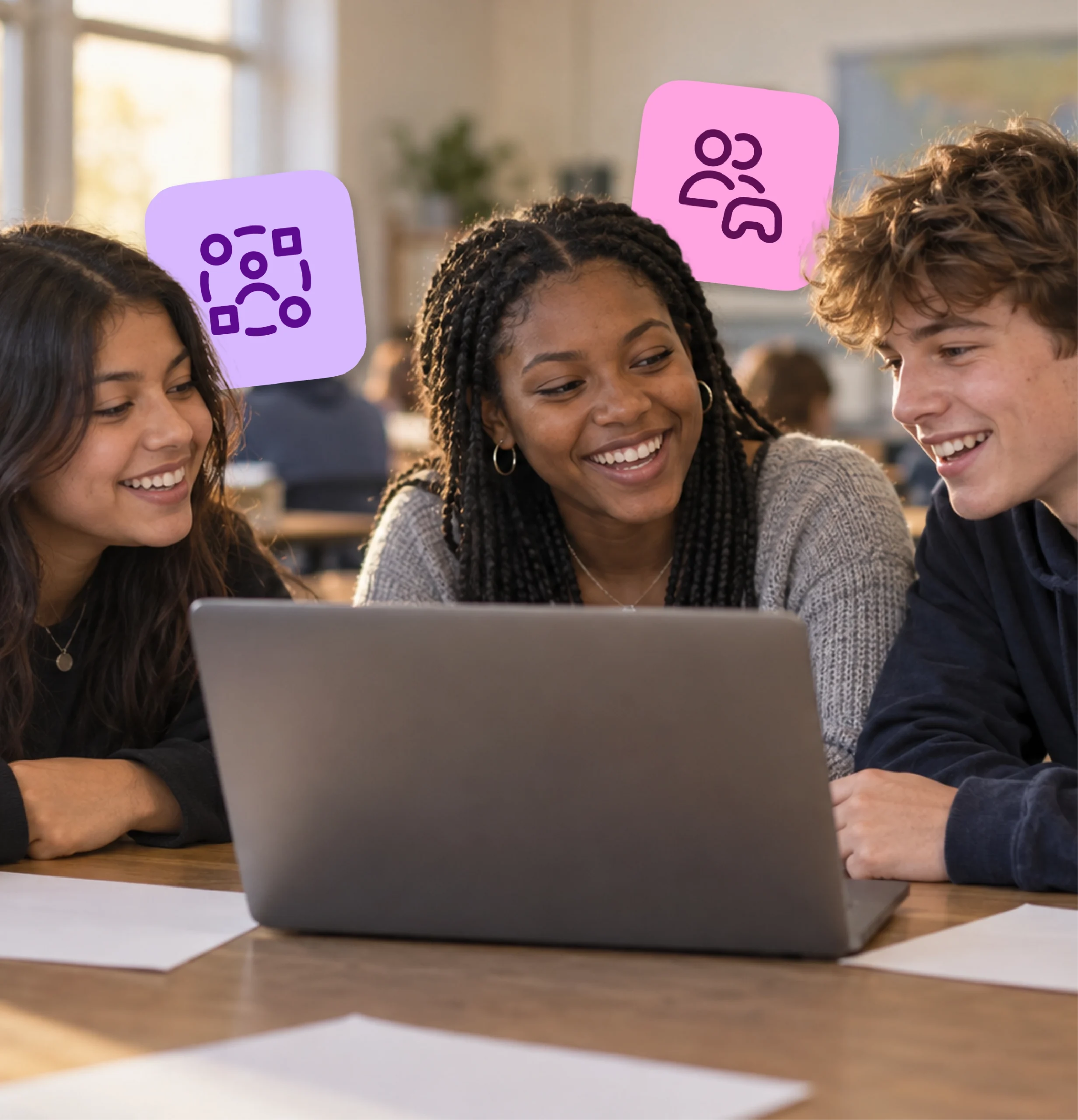 Three high school students laugh and talk together around a shared laptop.