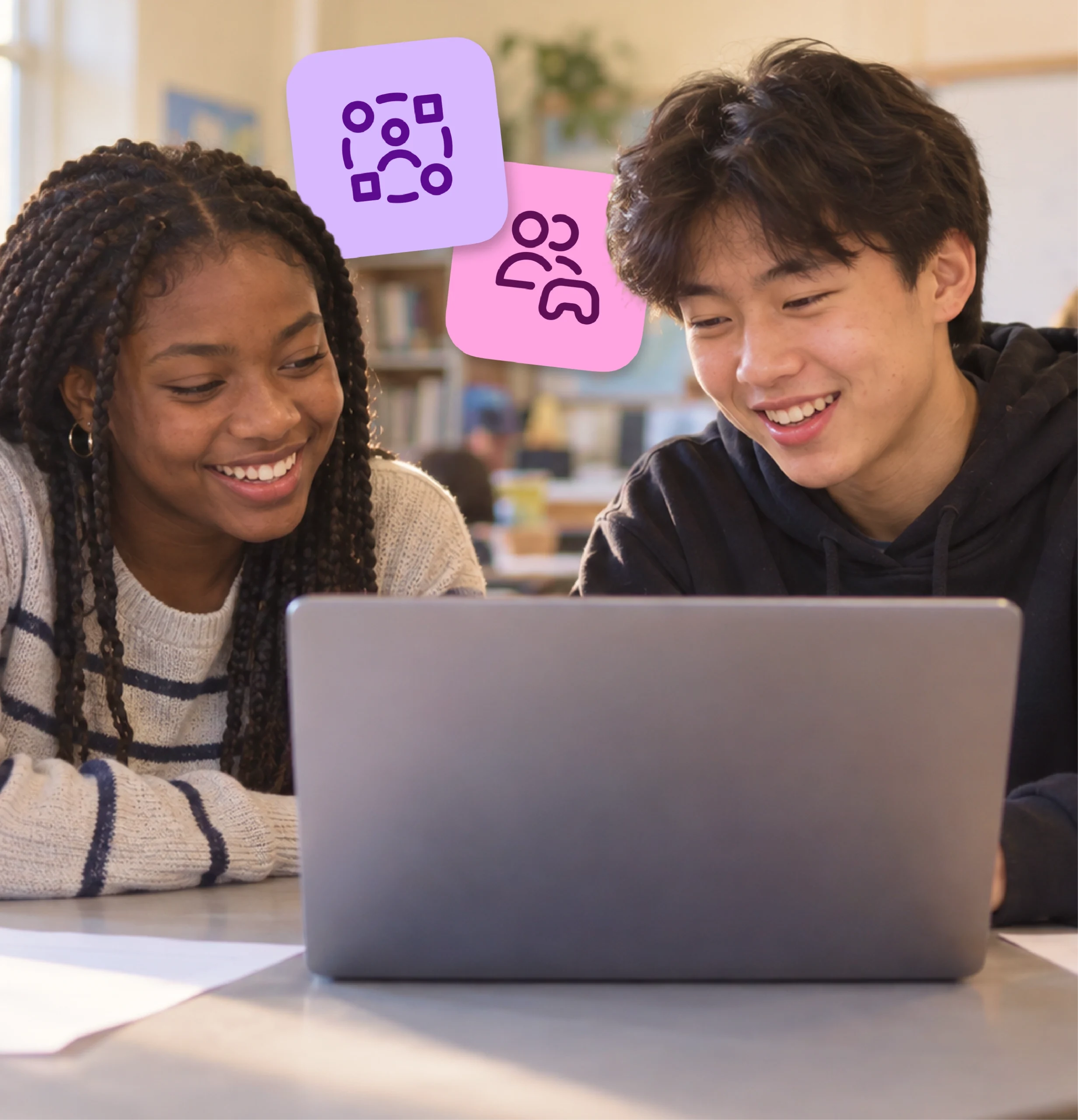 Two high school students smile as they work together on a shared laptop.