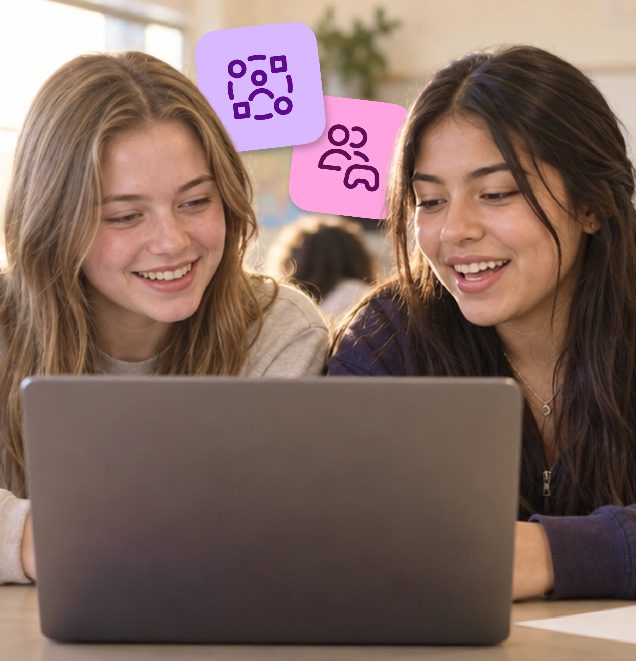 Two high school girls laugh together as they work on a shared laptop.