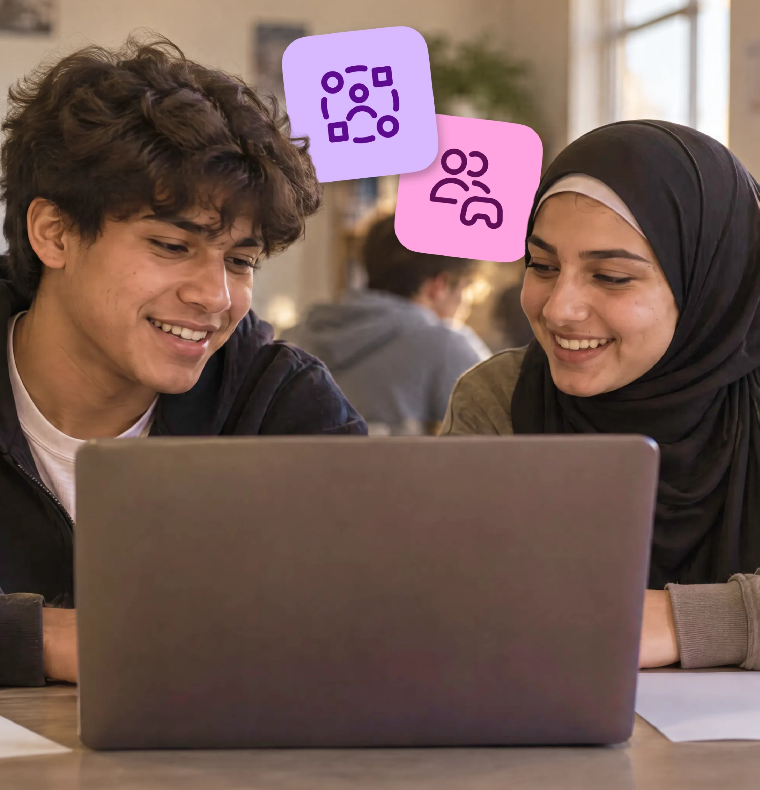 Two high school students smile and talk as they work together on a shared laptop.