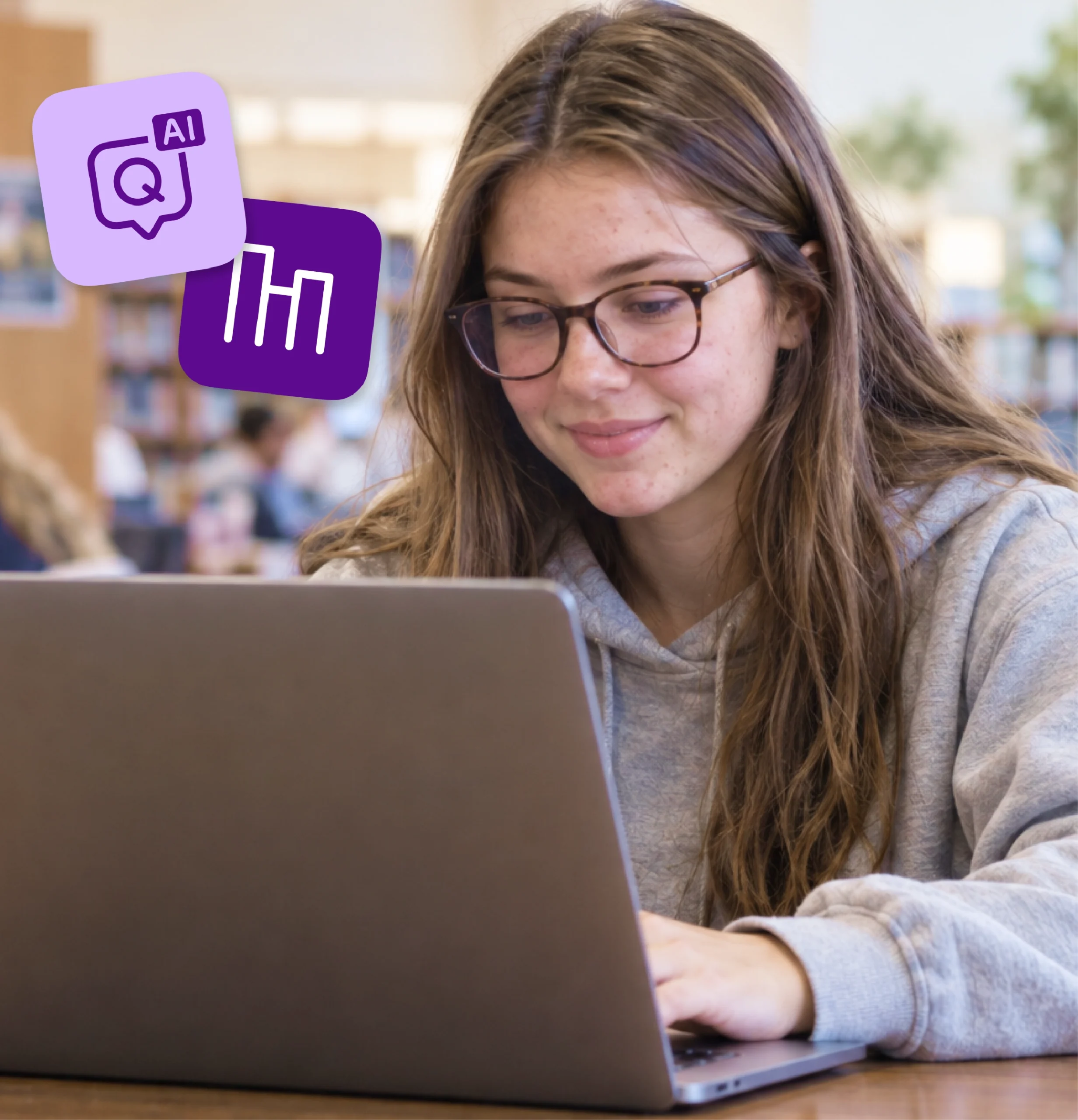A high school student smiles as she works on a laptop in the school library.